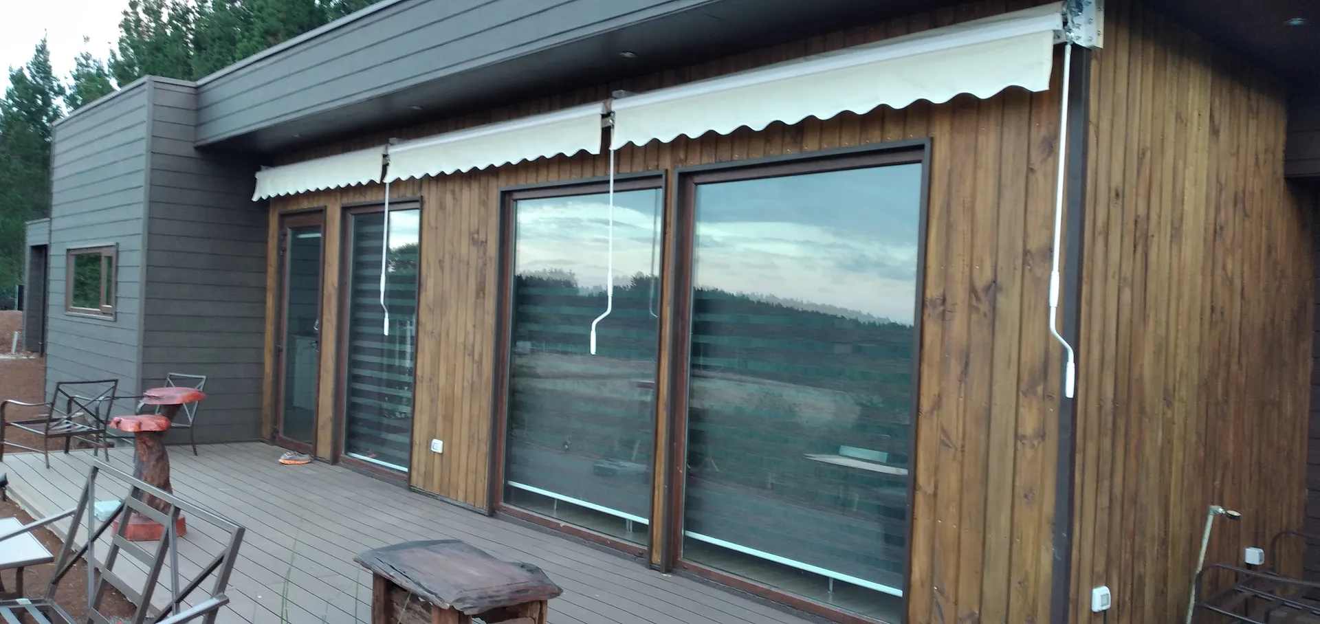 Toldo retráctil sobre los ventanales de una casa con revestimiento de madera